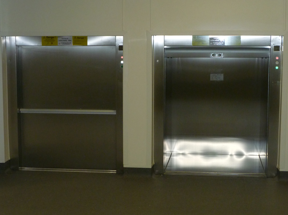 A pair of floor level loading dumbwaiter service lifts