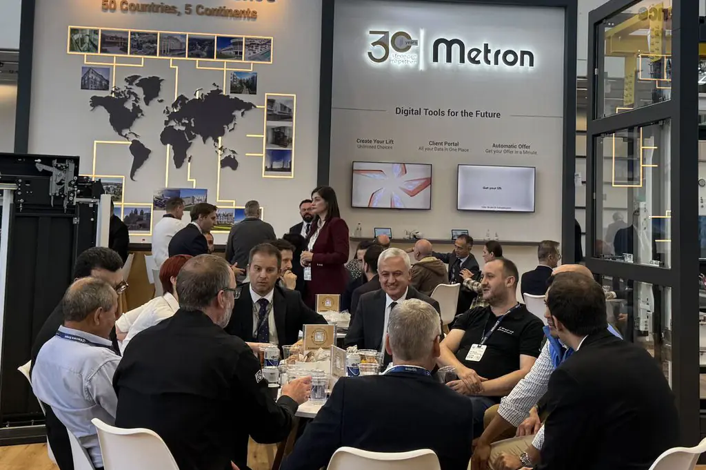 A group of people seated around a table in a conference setting, with displays in the background.