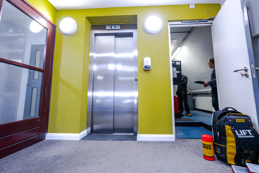 A brightly coloured hallway featuring an elevator, with a person holding a clipboard nearby.