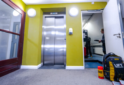 A brightly coloured hallway featuring an elevator, with a person holding a clipboard nearby.