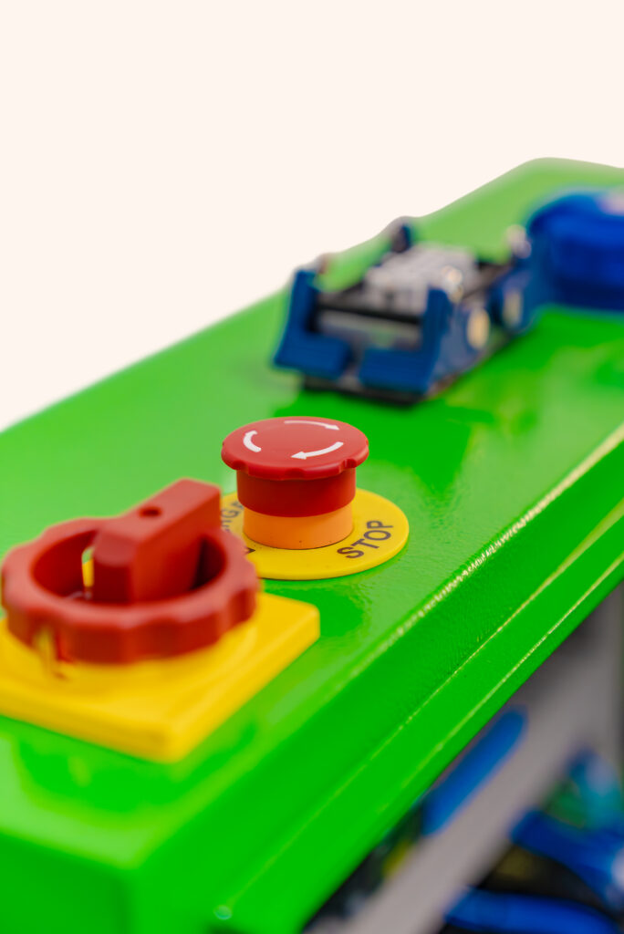 Close-up of a green control panel featuring various buttons, including a red emergency stop button.
