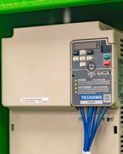 Yaskawa GA500 drive with control panel and blue wiring mounted on a green background.