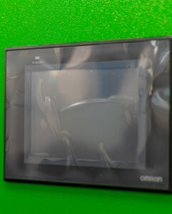 A touchscreen display mounted on a bright green wall, partially obscured by protective film.