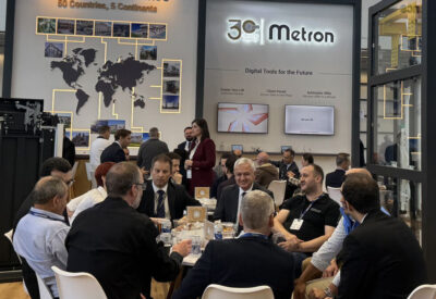 A group of people seated around a table in a conference setting, with displays in the background.